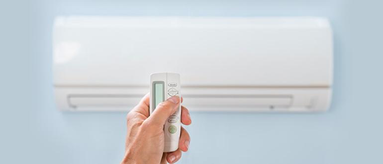 Zoom sur une main tenant une télécommande avec une climatisation fixée au mur en fond