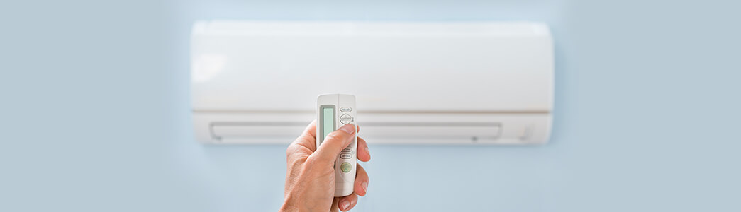 Zoom sur une main tenant une télécommande avec une climatisation fixée au mur en fond